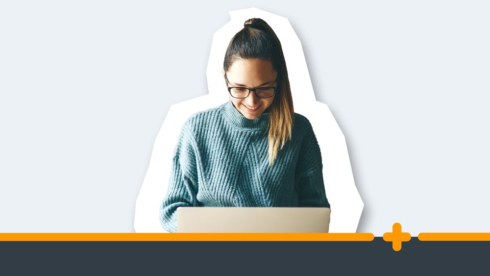 Młoda uśmiechnięta kobieta w okularach i swetrze pracująca przy laptopie