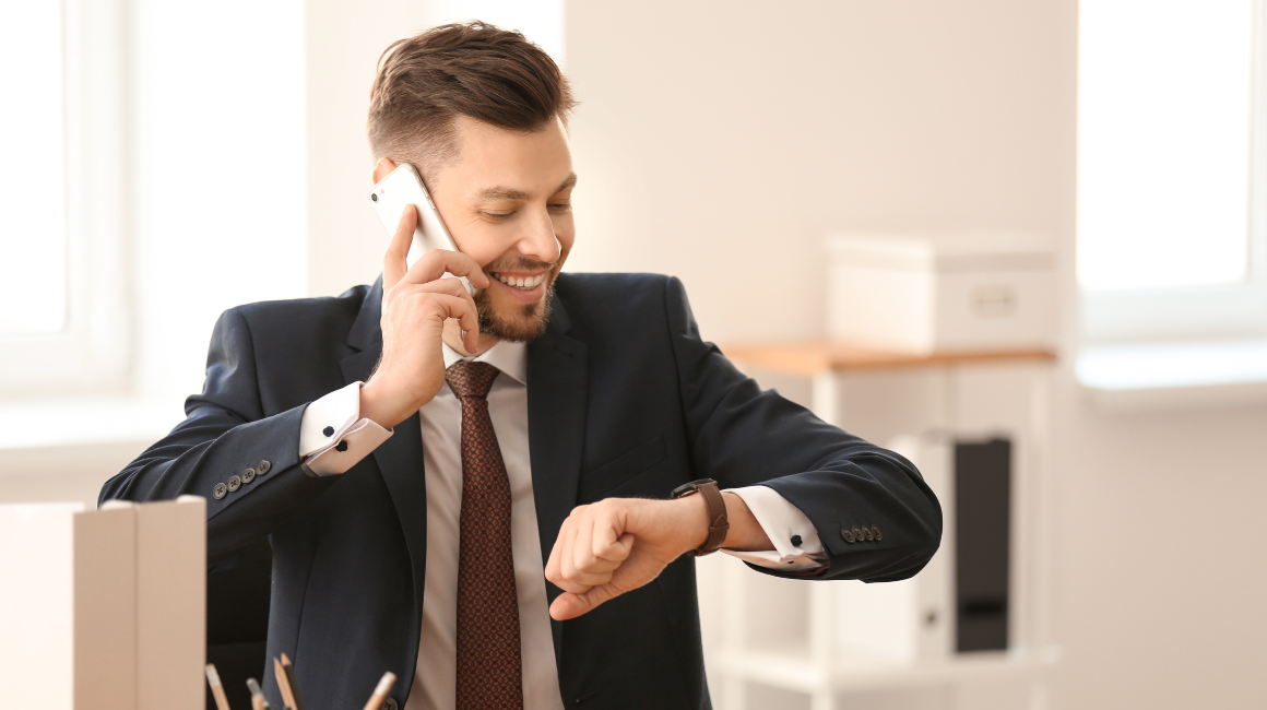Biznesmen w garniturze, siedzący w biurze, rozmawiający przez telefon i patrzący na zegarek